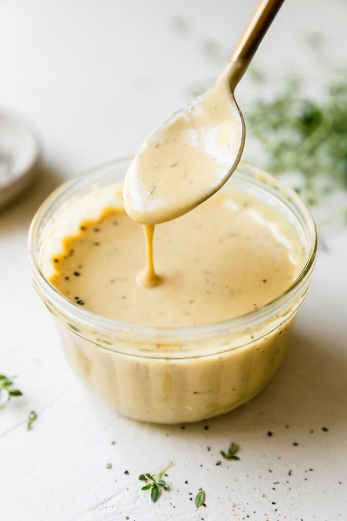 Homemade honey mustard sauce in clear bowl with spoonful of sauce hovering over dish.