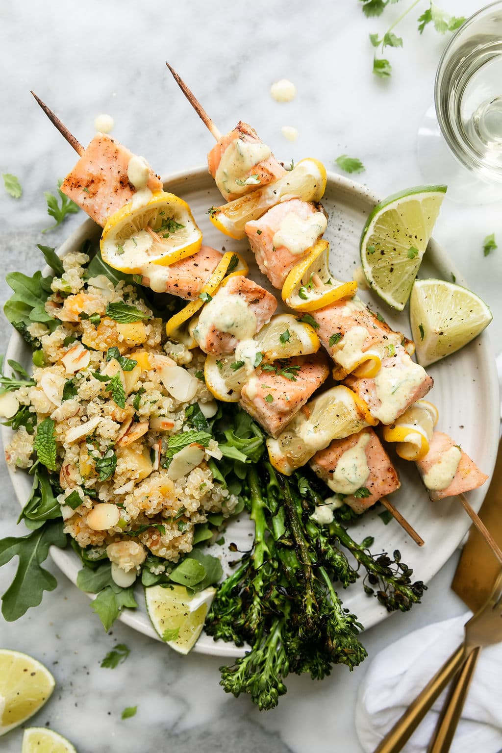 Plate with two grilled salmon kabobs with lemon, quinoa pilaf and curry yogurt sauce. 