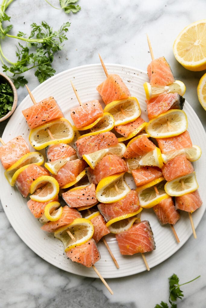 Overhead view five skewers with salmon pieces and lemon slices threaded on.