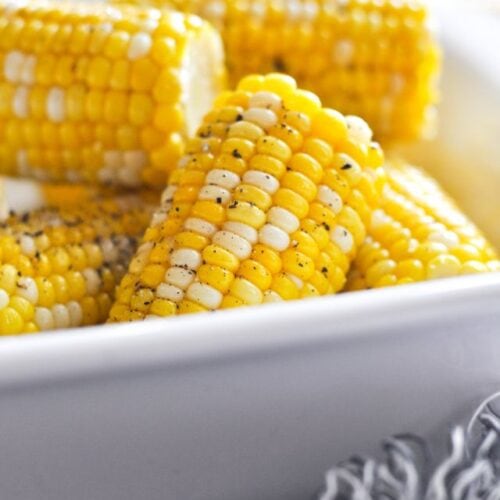 Instant Pot corn on the cob halves in white serving dish with black pepper sprinkled over top.