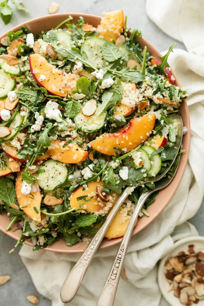 Close up view peach and arugula quinoa salad with toasted almonds and goat cheese crumbles.