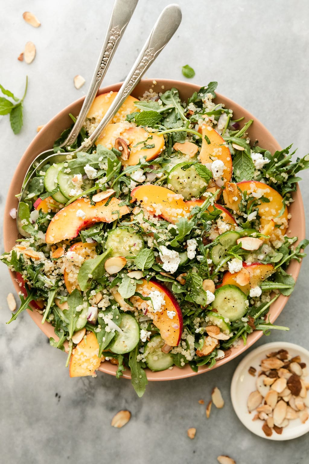 Overhead view quinoa arugula salad with peaches and goat cheese crumbles in pink bowl.