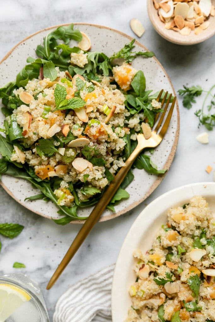 Plate full of herbed quinoa pilaf with apricots and almonds served over arugula. 