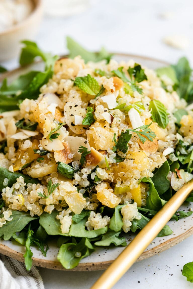 Close up view herbed quinoa pilaf served over arugula with apricots and almonds.