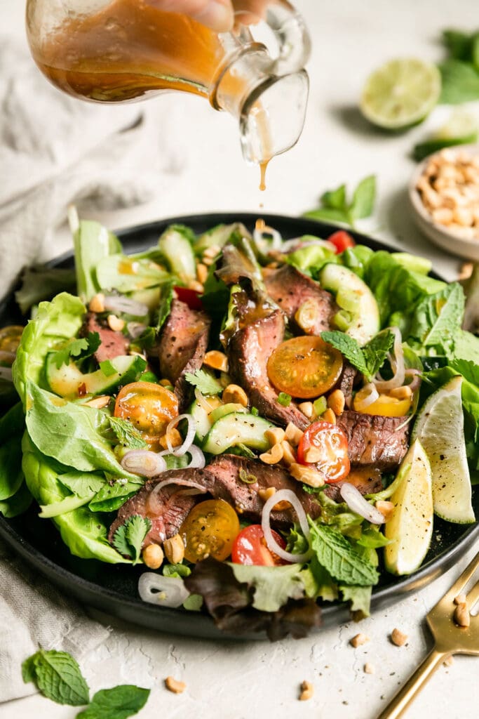 Steak salad served on a black plate with salad dressing being poured over top. 