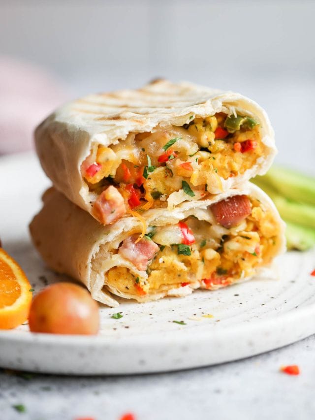 A cut in half breakfast burrito with scrambled eggs and ham stacked up on each other.