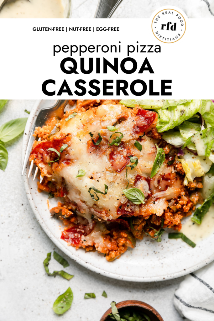 Serving of pepperoni pizza quinoa casserole topped with melted mozzarella cheese on stone plate with serving of side salad.