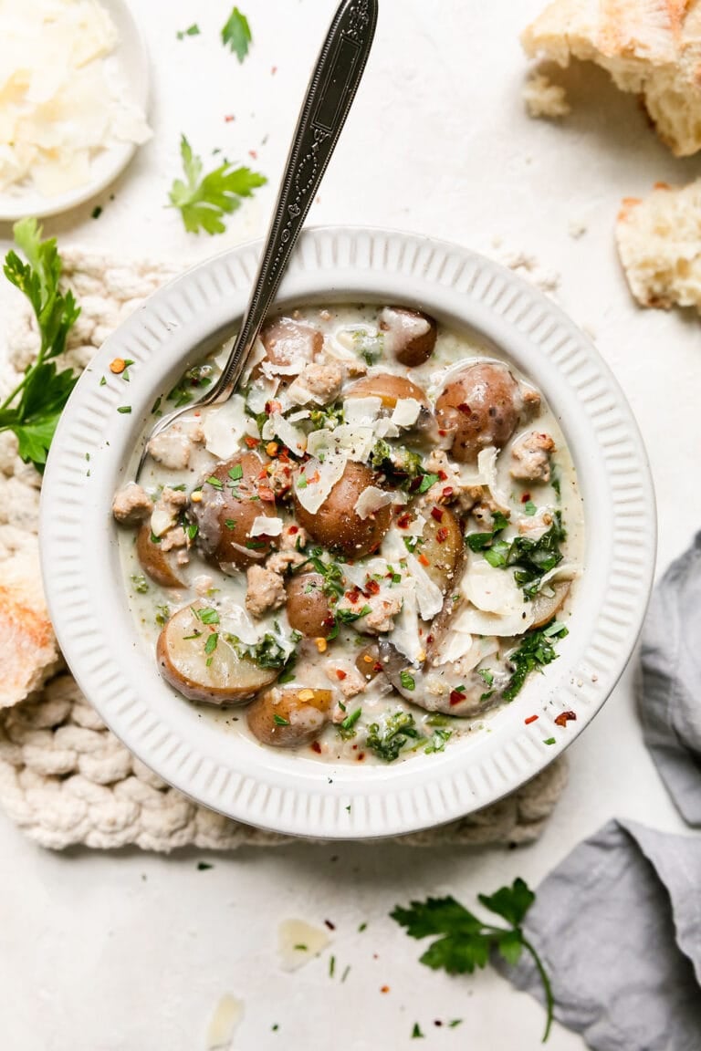 Overhead view of a bowl of zuppa Toscana soup topped with red pepper flakes and shaved parmesan. 