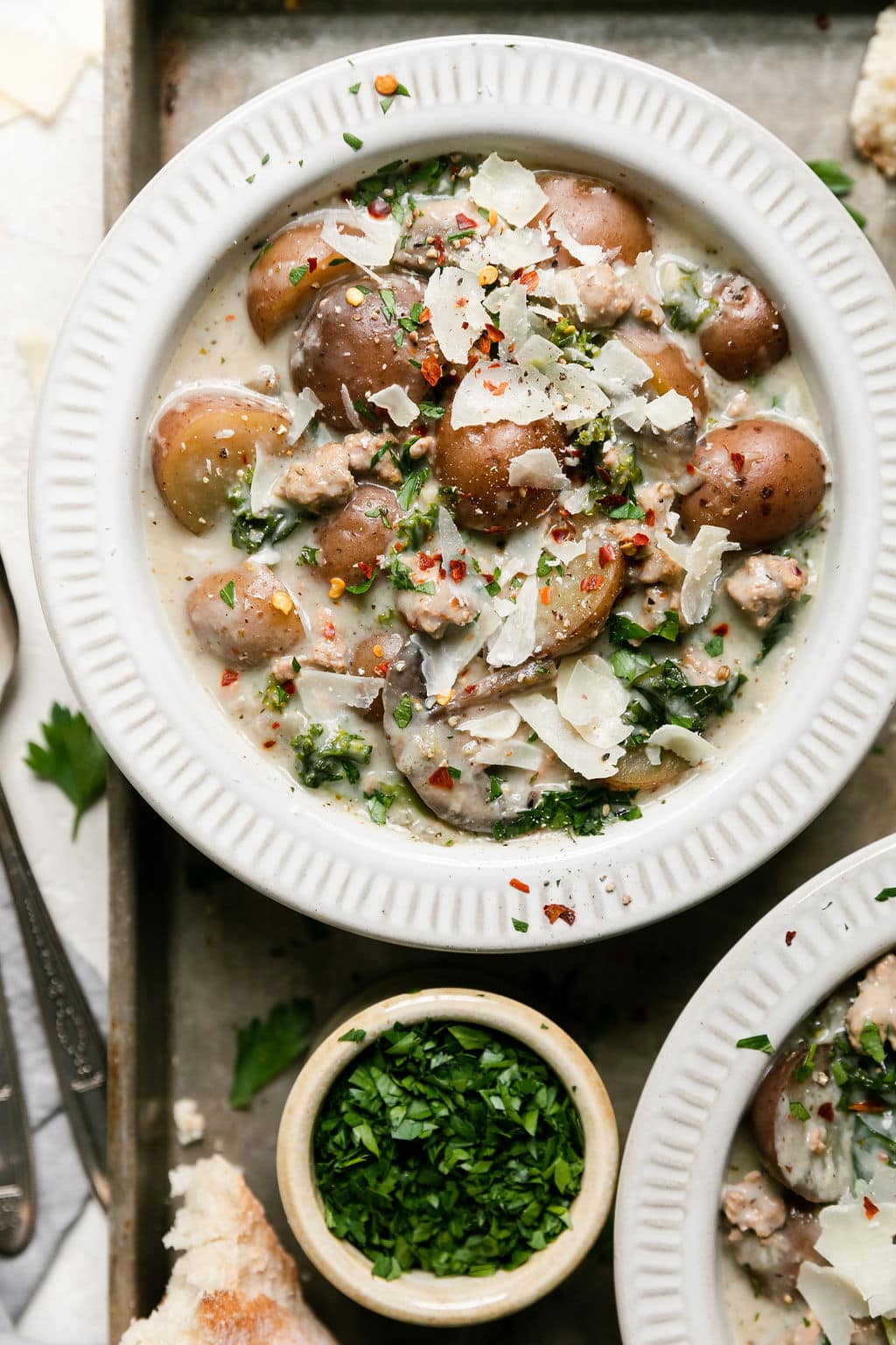 Overhead view Zuppa Toscana soup in white bowl topped with shaved Parmesan cheese and red pepper flakes.
