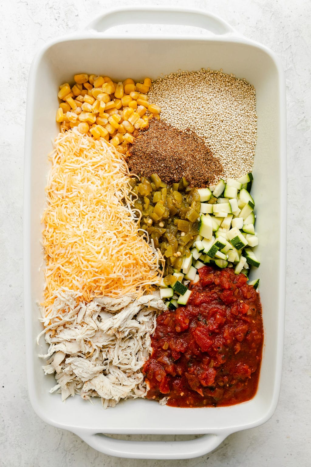 All ingredients for chipotle quinoa casserole in a white baking dish ready to stir together.