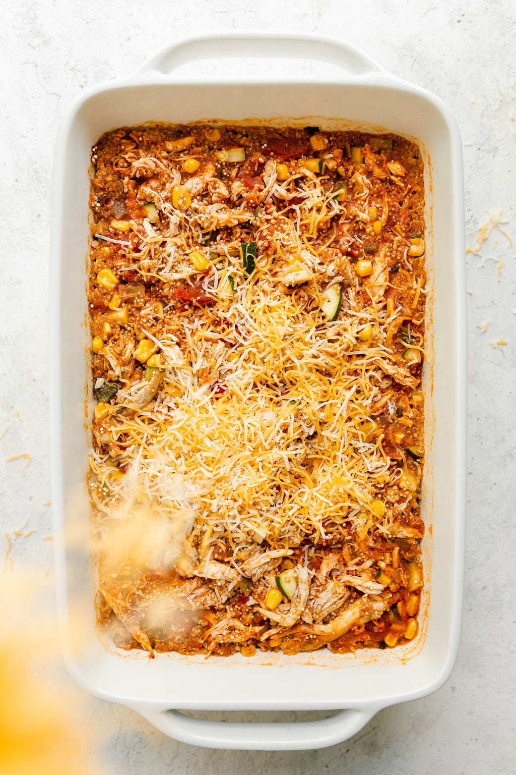 Chipotle quinoa casserole with chicken in a white baking dish with cheddar cheese being sprinkled on top.