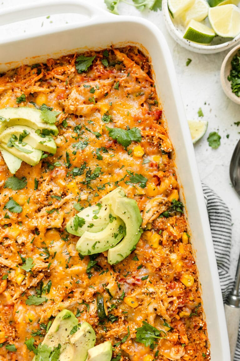 Chipotle flavored quinoa casserole with chicken and corn in baking dish topped with melted cheddar cheese, avocado slices and fresh cilantro.