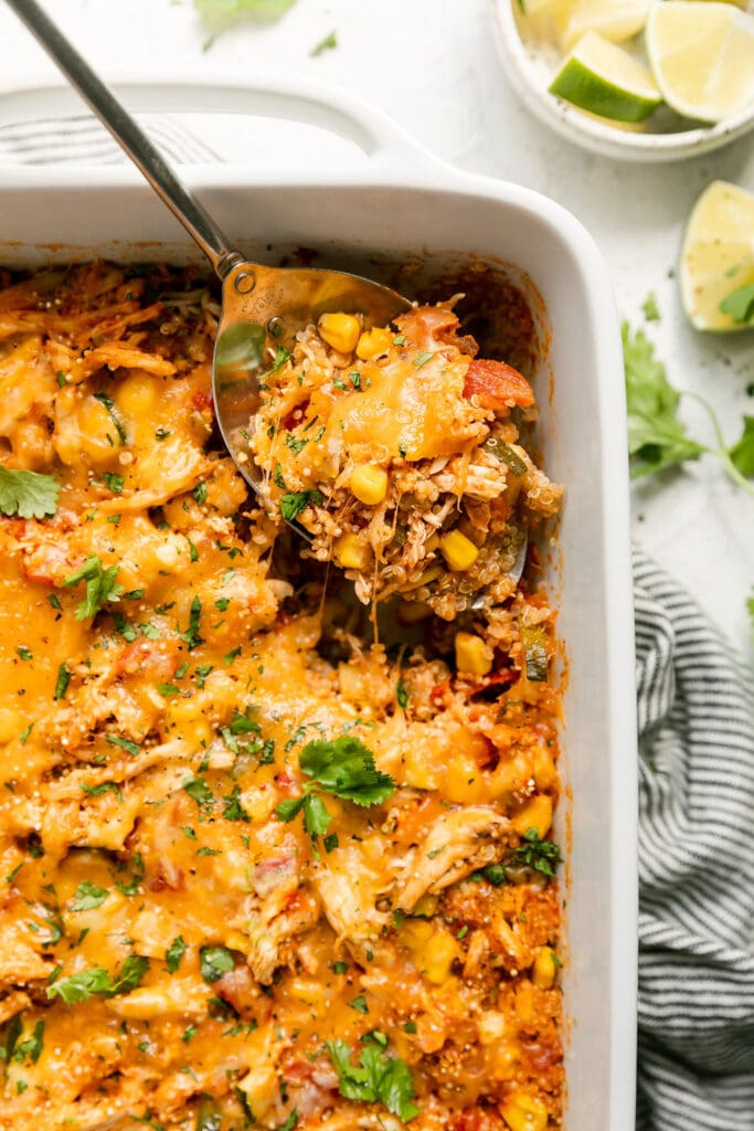 A spoonful of chipotle quinoa casserole with chicken and cheddar cheese being lifted from a white casserole.