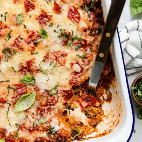 Pepperoni pizza quinoa casserole in baking dish with spoon in casserole for serving.
