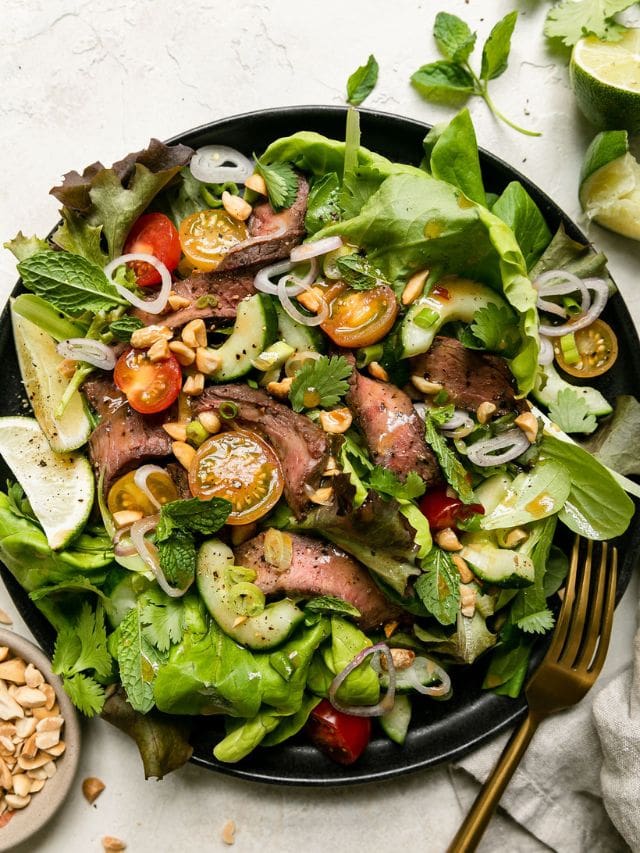 Overhead view Thai-inspired steak salad on a black plate.