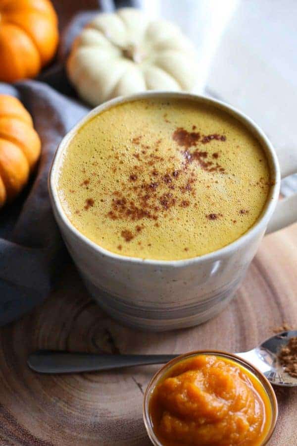 A mug filled with pumpkin spice butter coffee, small pumpkins in the background.