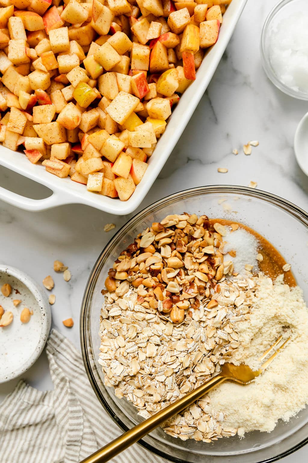 Diced apples with cinnamon in a white baking dish, a mixing bowl filled with ingredients for peanut butter and oat topping.
