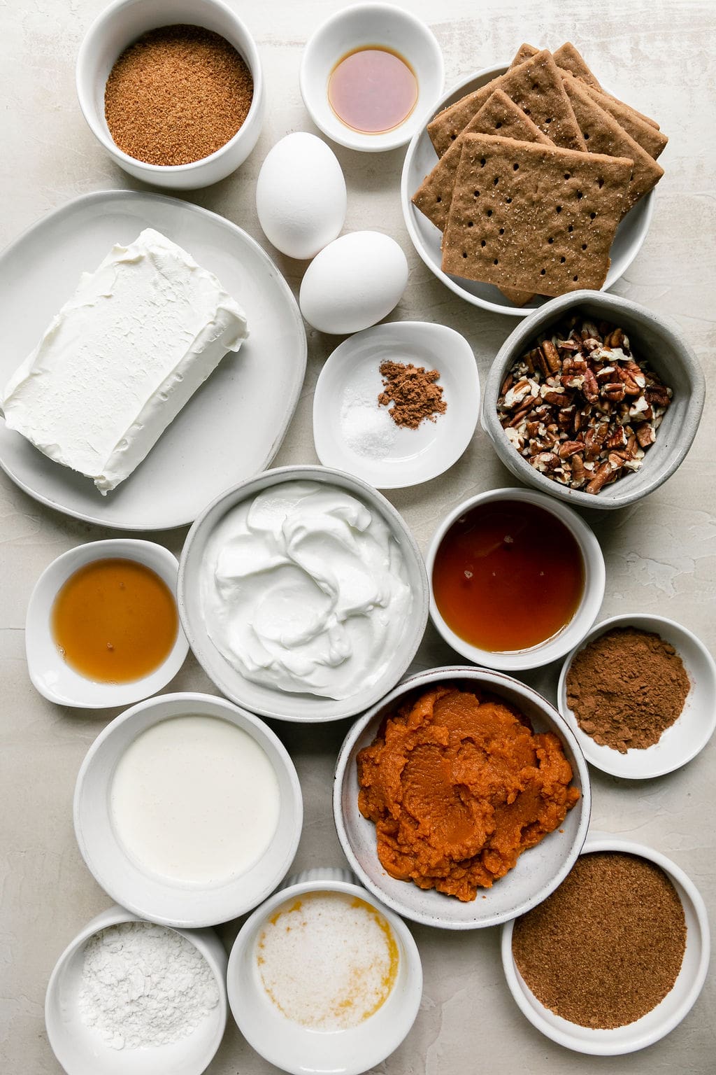 All ingredients for mini pumpkin cheesecake bars arranged together in small bowls and plates.