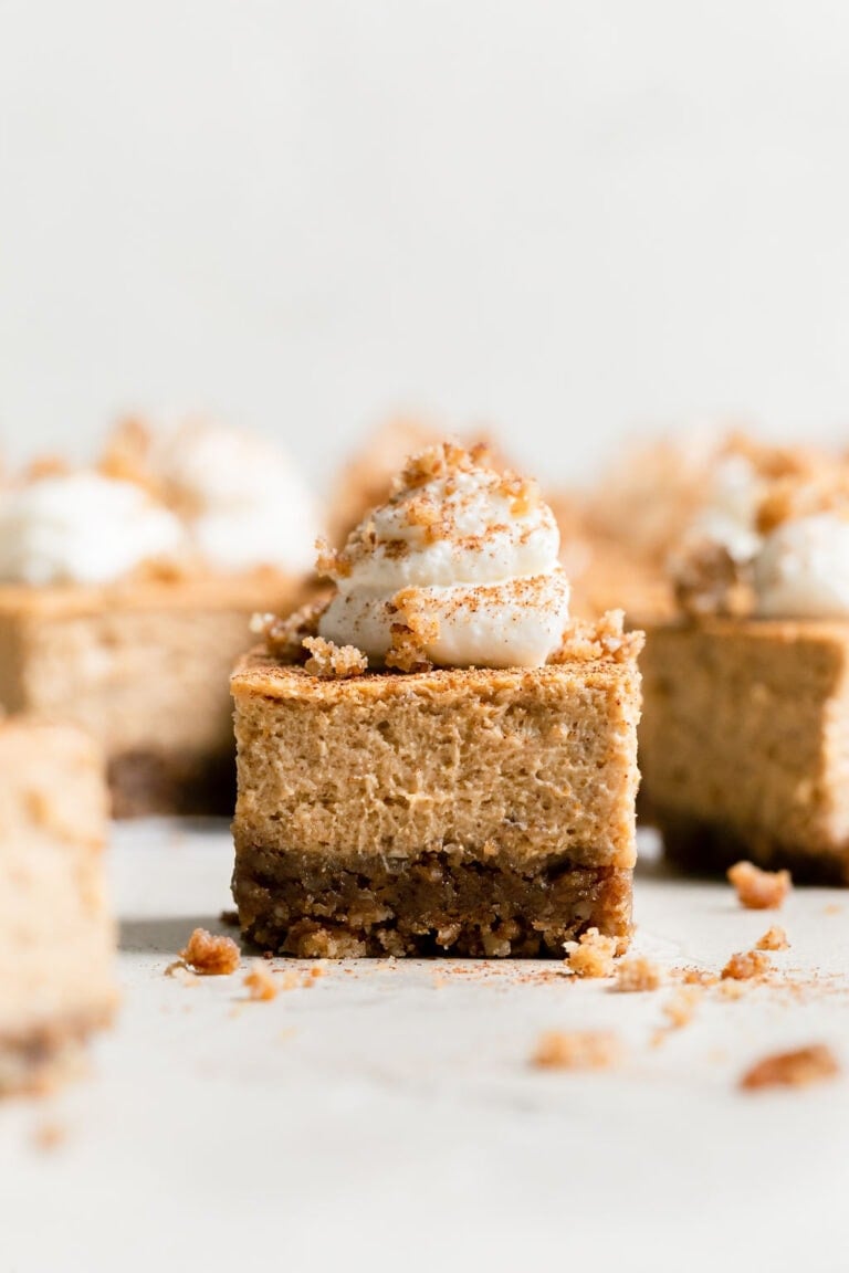 A mini pumpkin cheesecake bar topped with whipped cream.