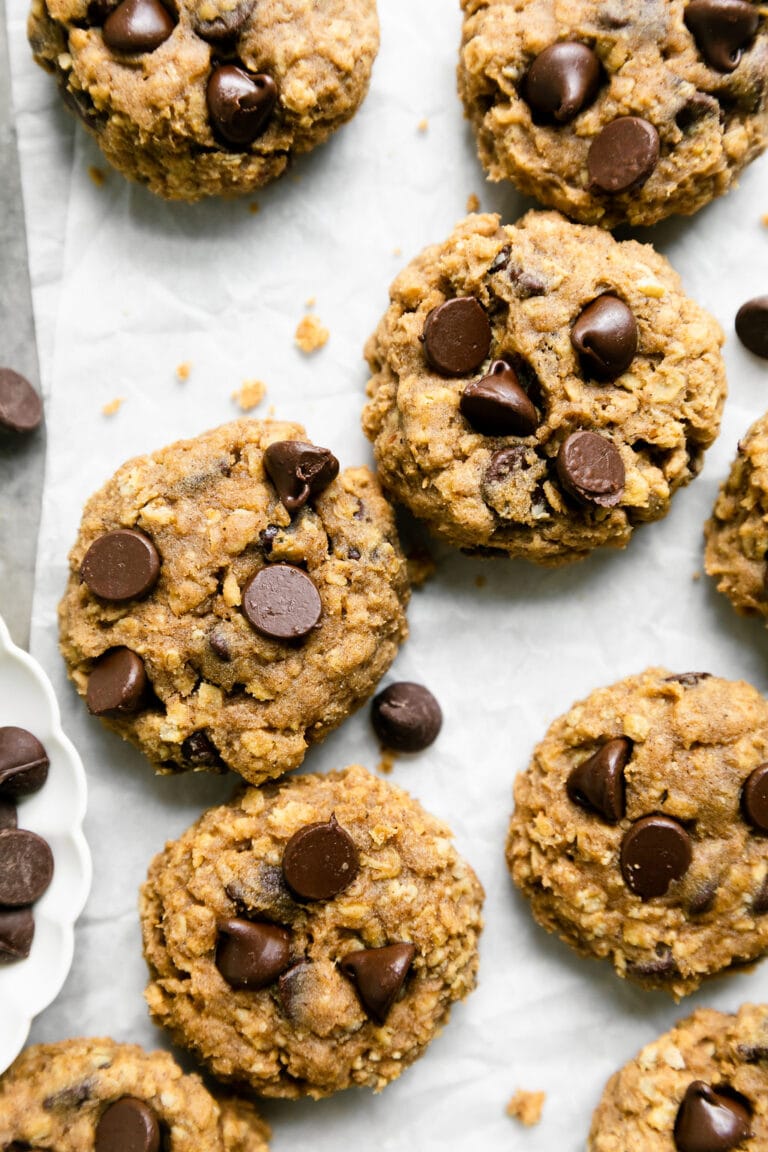 Overhead view of a batch of freshly baked oatmeal pumpkin chocolate chip cookies on parchment paper.