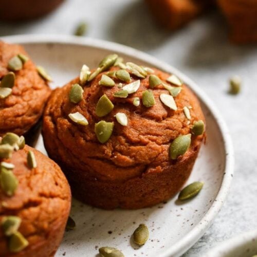 Close up side view pumpkin protein muffins topped with pepita pieces.