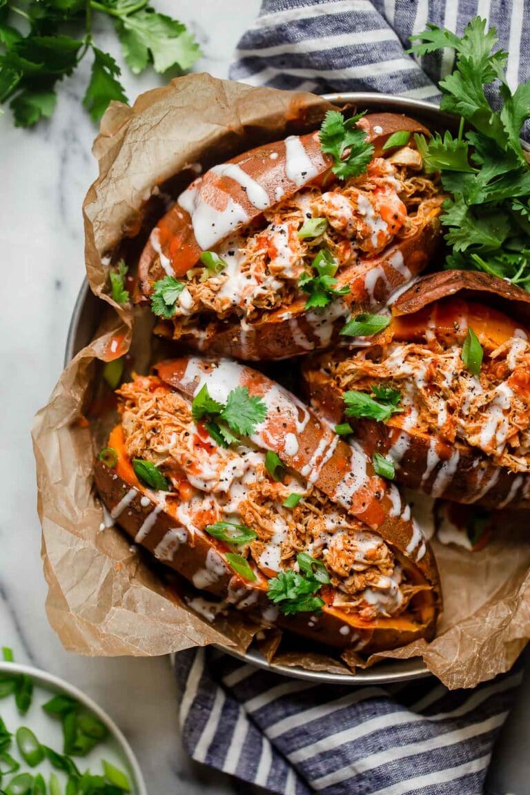Overhead view three buffalo chicken stuffed sweet potatoes in parchment covered round tray.