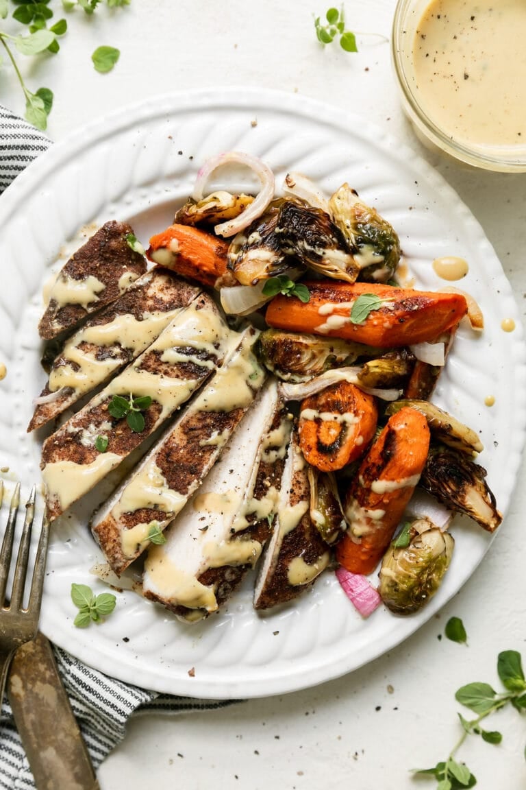 A white plate filled with roasted chicken and vegetables including caramelized red onion and topped with a maple Dijon dressing. 