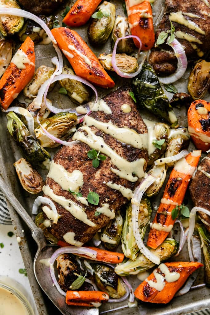Close up overhead view harvest chicken dinner with roasted vegetables on sheet pan, drizzled with maple dijon dressing.