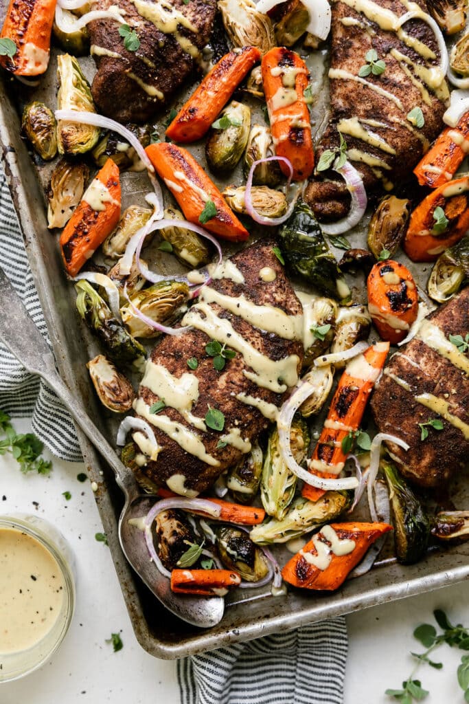 overhead view sheet pan chicken and roasted veggies coated in seasoning and drizzled with maple dijon mustard.