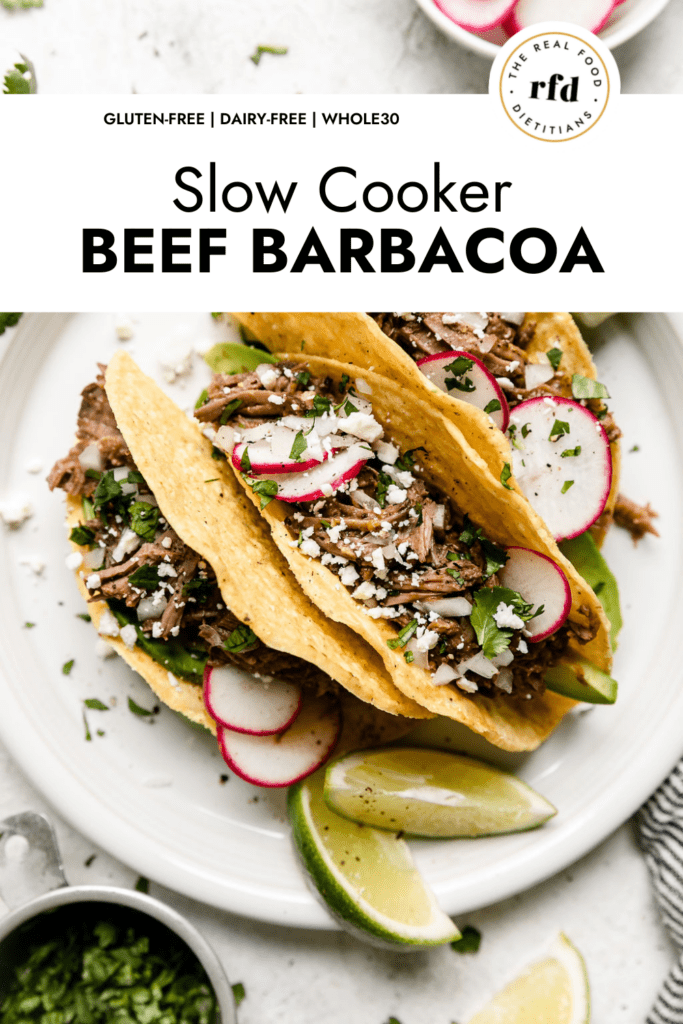 Overhead view slow cooker beef barbacoa tacos in hard shells with sprinkle of cheese and fresh cilantro over top.