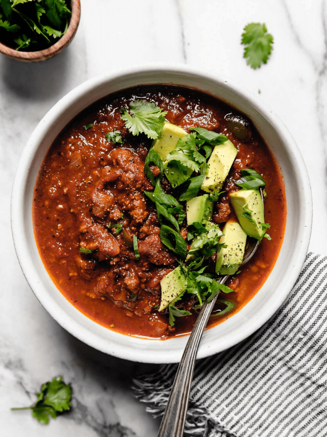 Overhead view white bowl filled with slow cooker pumpkin chili topped with diced avocado and sliced green onions.
