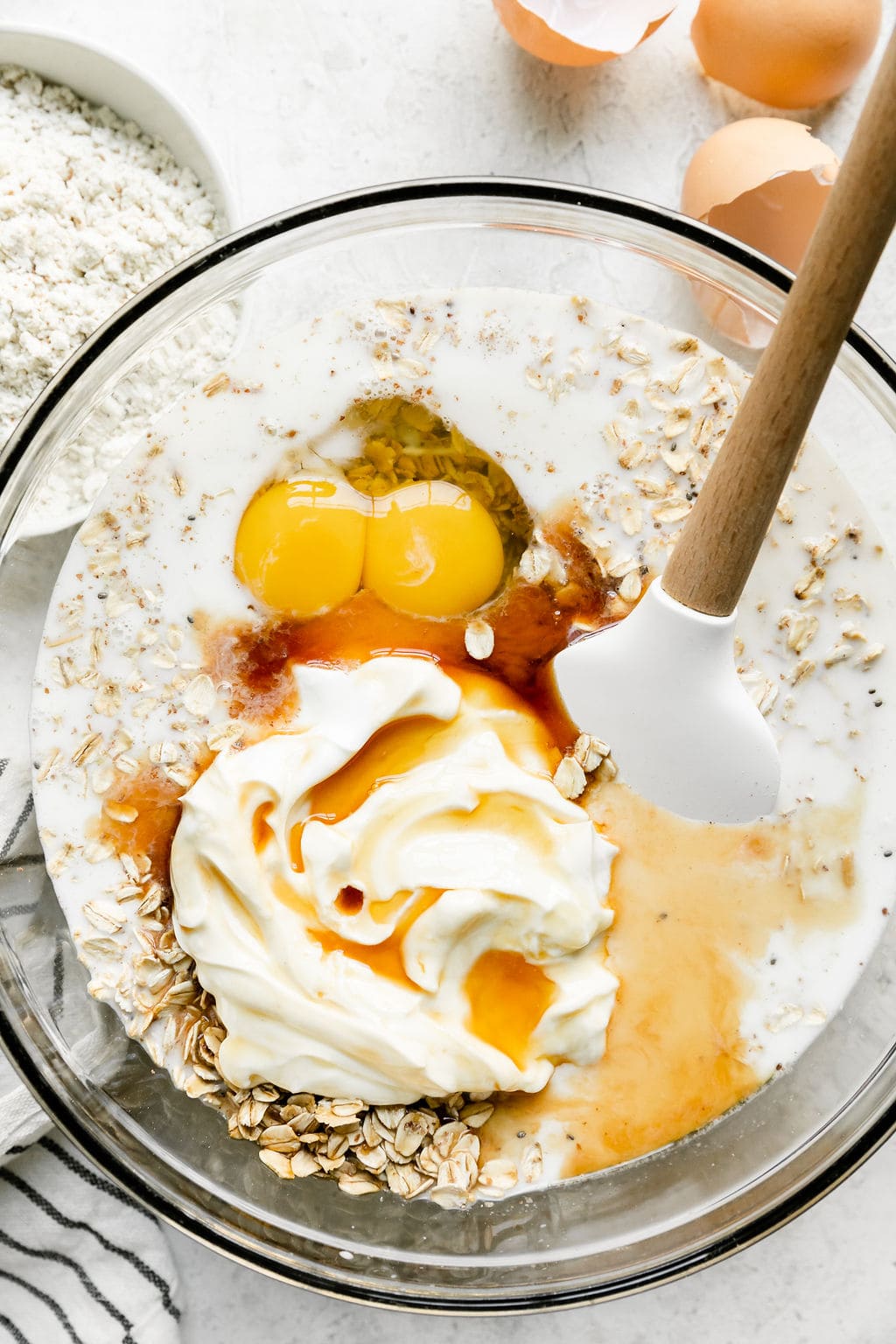 Close up view of baking ingredients being stirred in a glass bowl by wooden spatula.  