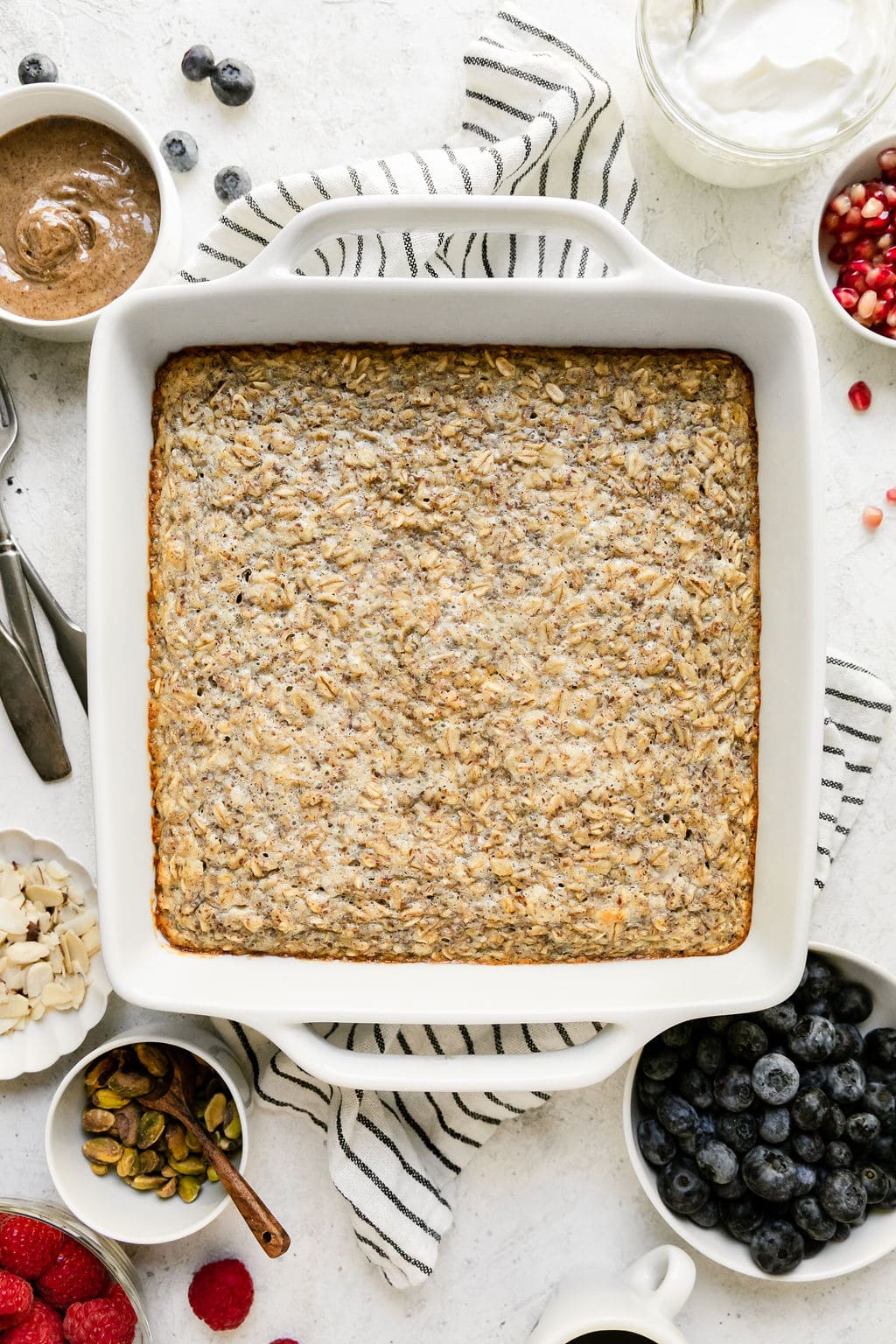 Overhead view white baking dish filled with protein baked oatmeal, side dishes with toppings on each side.