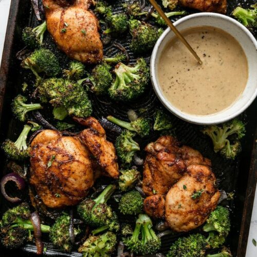 Overhead view sheet pan filled with chipotle chicken thighs, roasted broccoli and bowl with honey mustard sauce