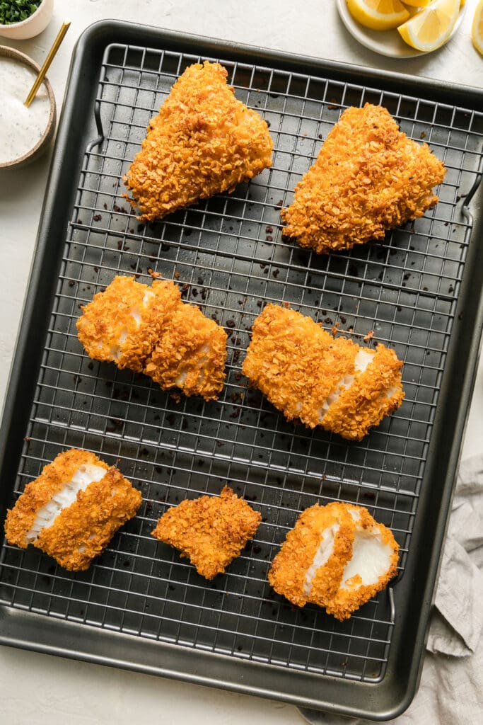 Overhead view seven cod fillets coated in crispy coating on wire rack baking sheet combo.