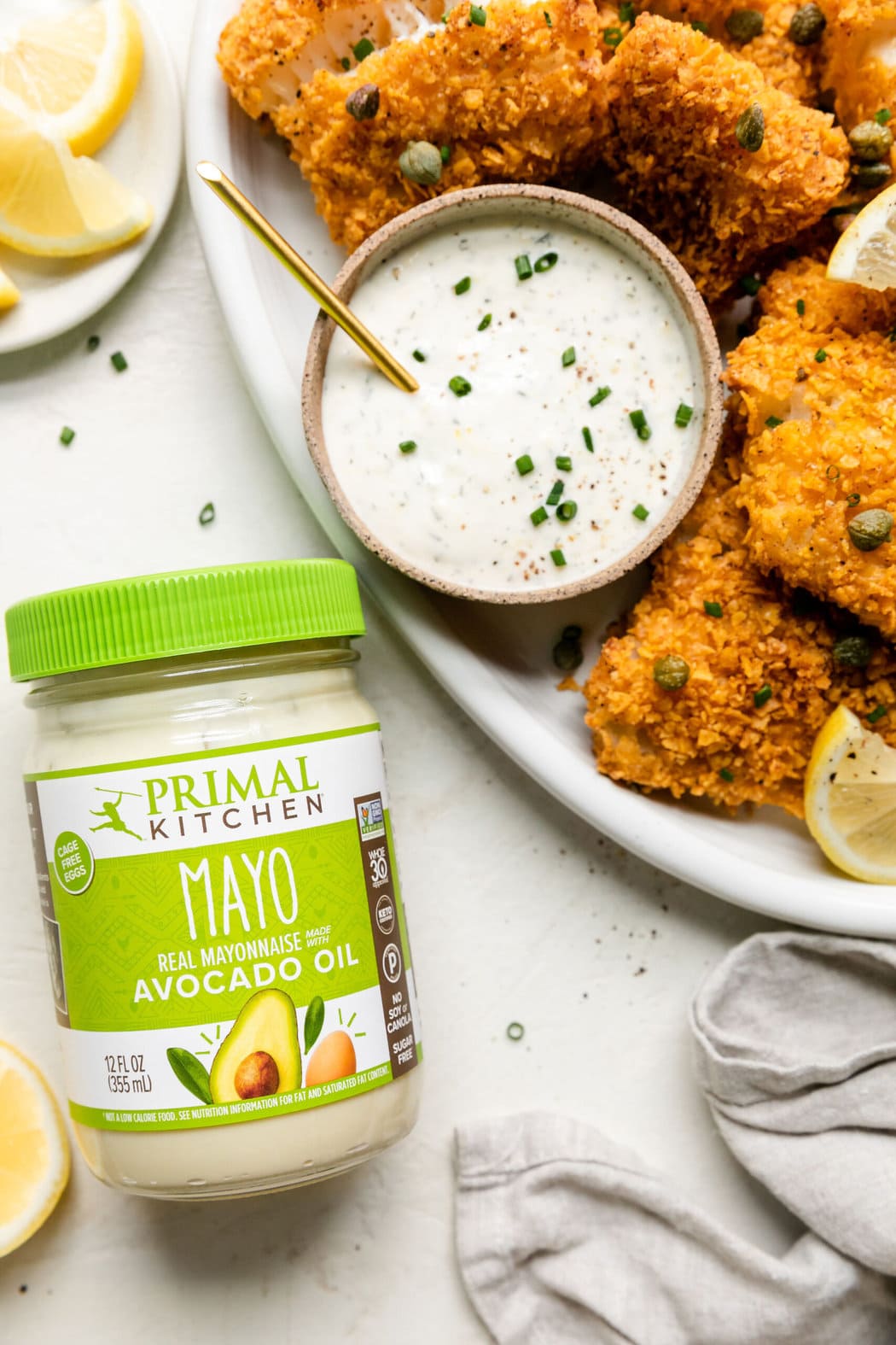 Crispy baked cod on white platter with small bowl aioli sauce, jar of Primal Kitchen mayonnaise next to platter.