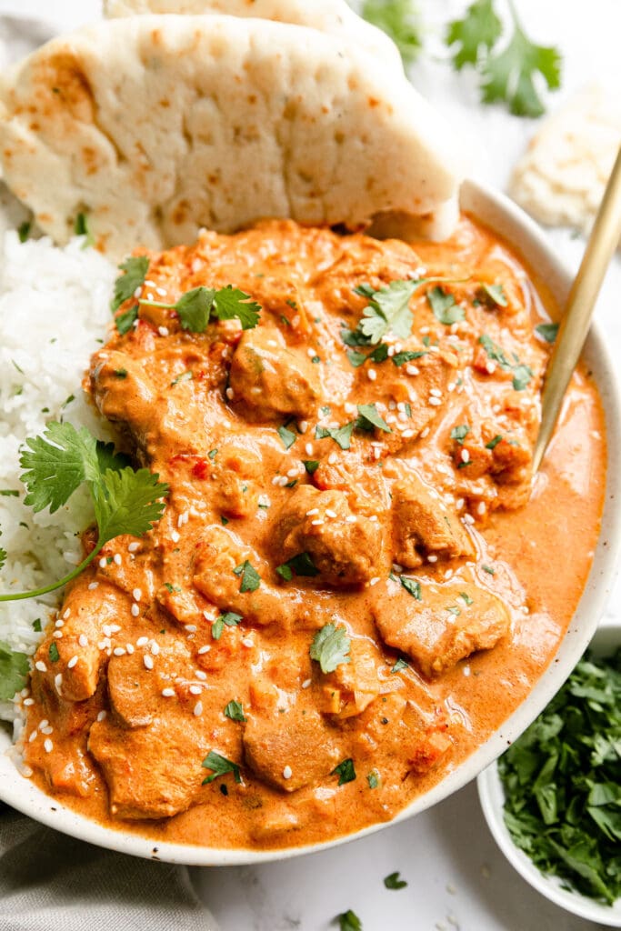 Serving of creamy crockpot butter chicken in stone bowl with white rice and naan bread.