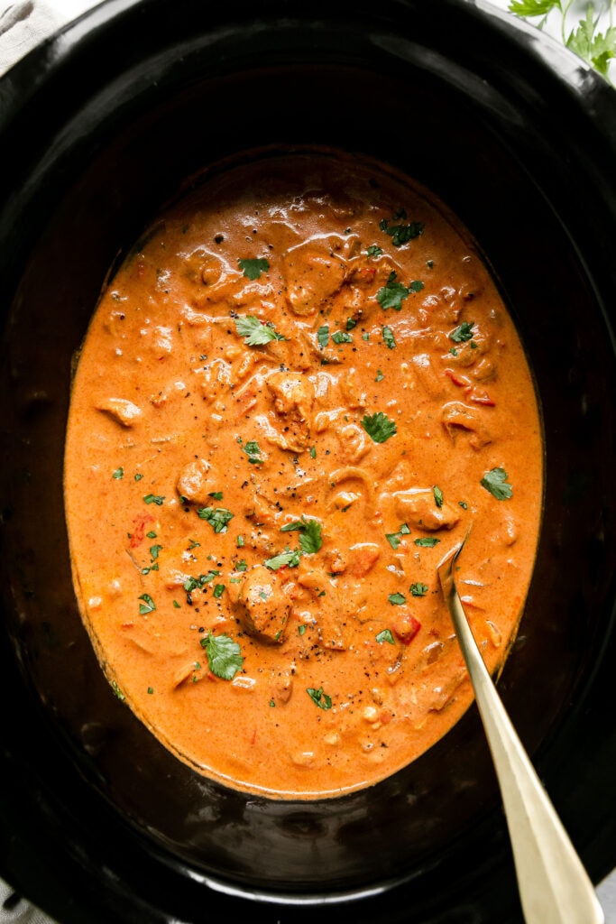 Overhead view black slow cooker filled with creamy butter chicken