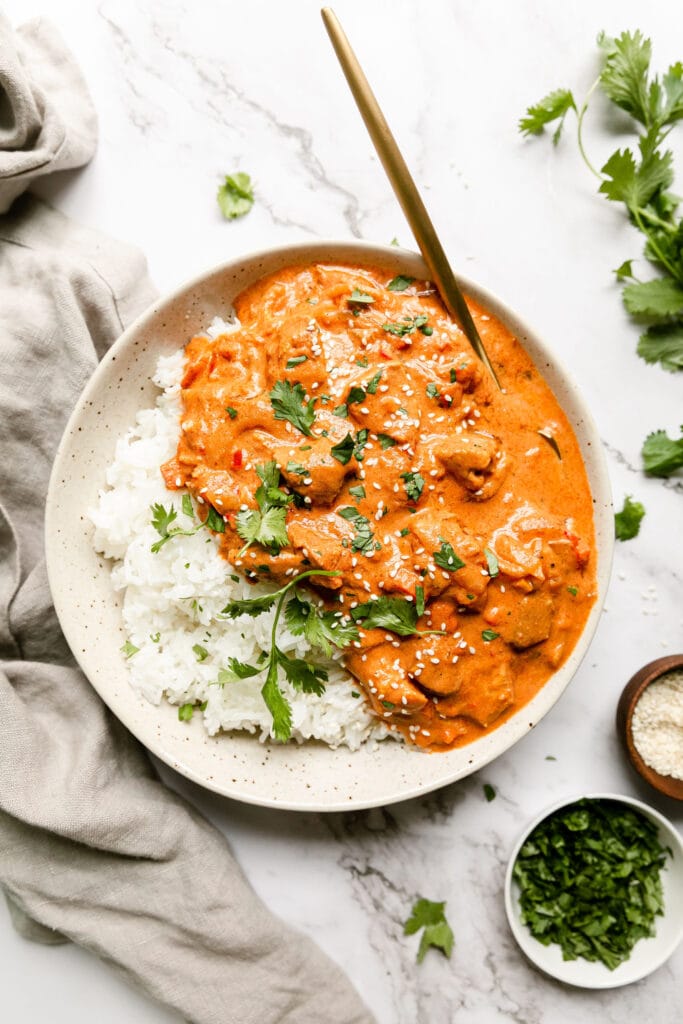 Stone bowl with serving of butter chicken in sauce served with white rice.