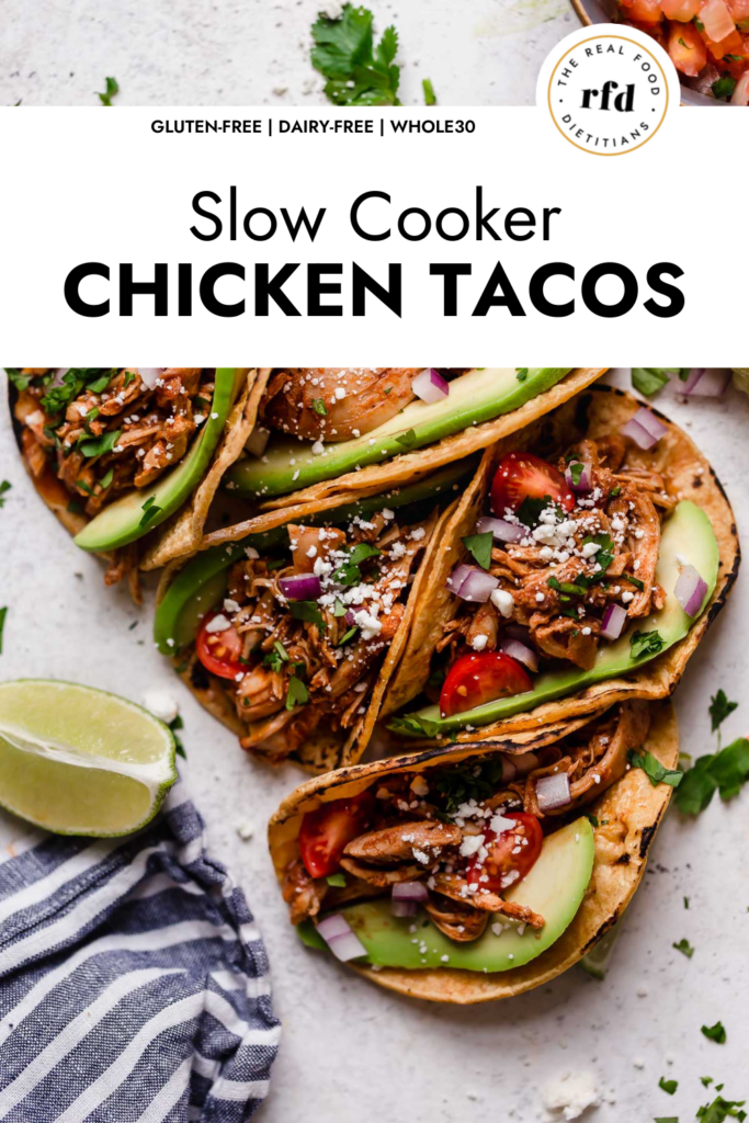 Slow cooker shredded chicken taco meat in corn shells with avocado slices and cojito cheese.