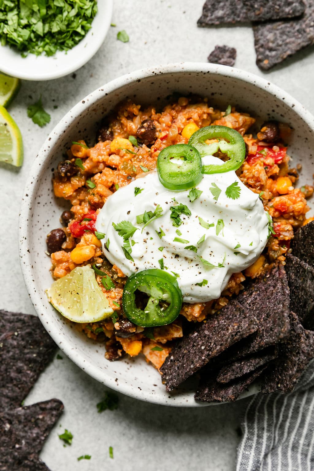 Serving of Southwest chicken quinoa casserole in bowl topped with sour cream and jalapeño slices, blue tortilla chips on the side.