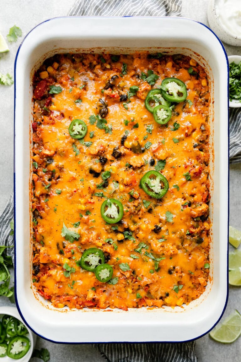 Overhead view white baking dish filled with Southwest chicken quinoa casserole topped with melted cheddar cheese and jalapeño slices. 