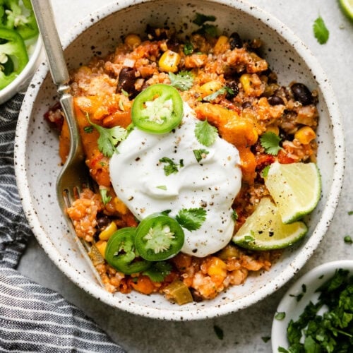 A serving of Southwest chicken quinoa casserole in a bowl topped with sour cream and jalapeño slices.