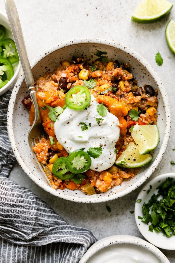 A serving of Southwest chicken quinoa casserole in bowl topped with sour cream and jalapeño slices. 