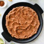 Black round tray with layer of refried beans spread in circle for 7 layer dip.