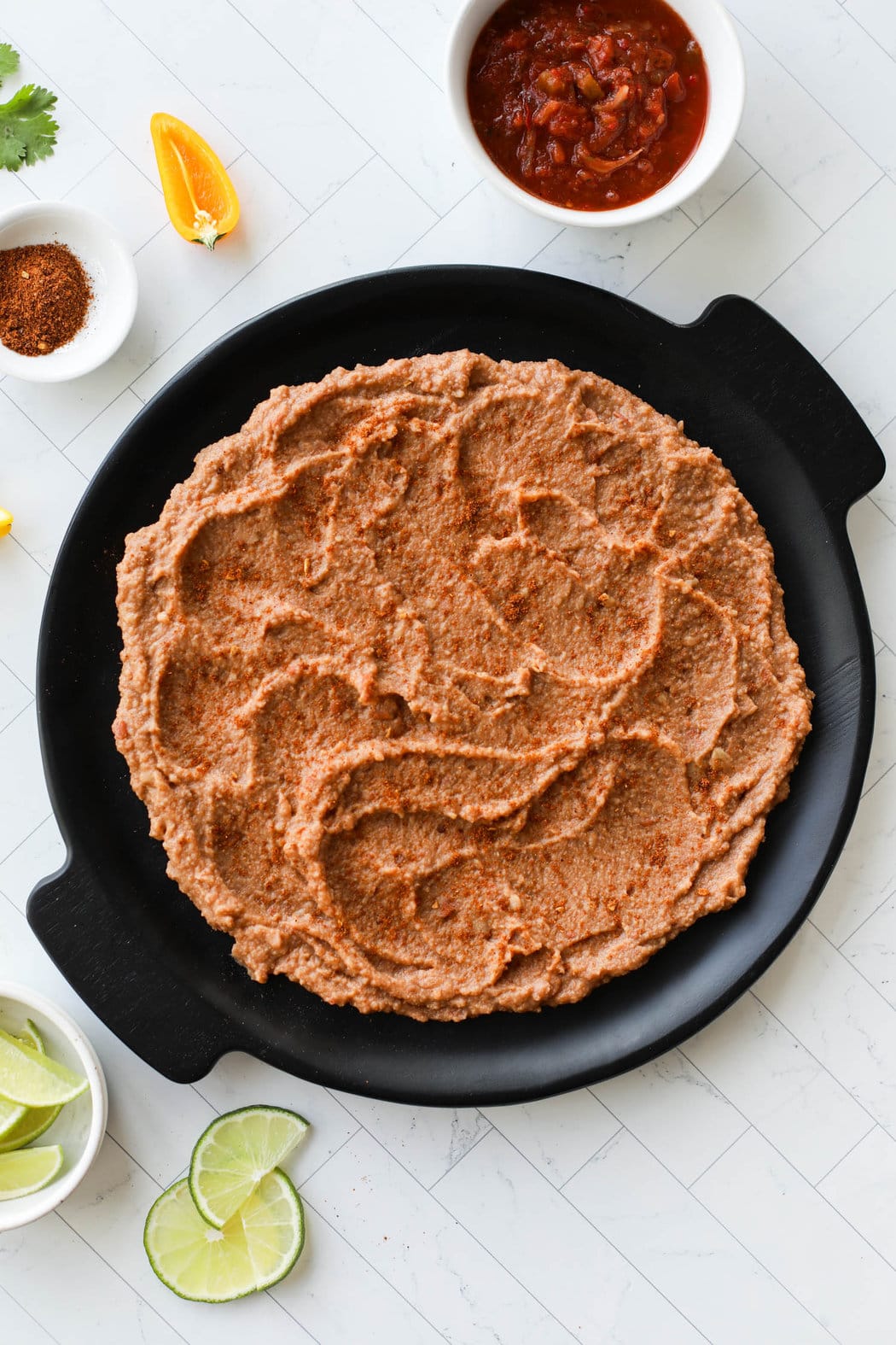 Black platter with refried beans spread on circle for bottom layer of 7 layer dip.