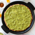 Black round tray with layer of refried beans and guacamole spread in a circle.
