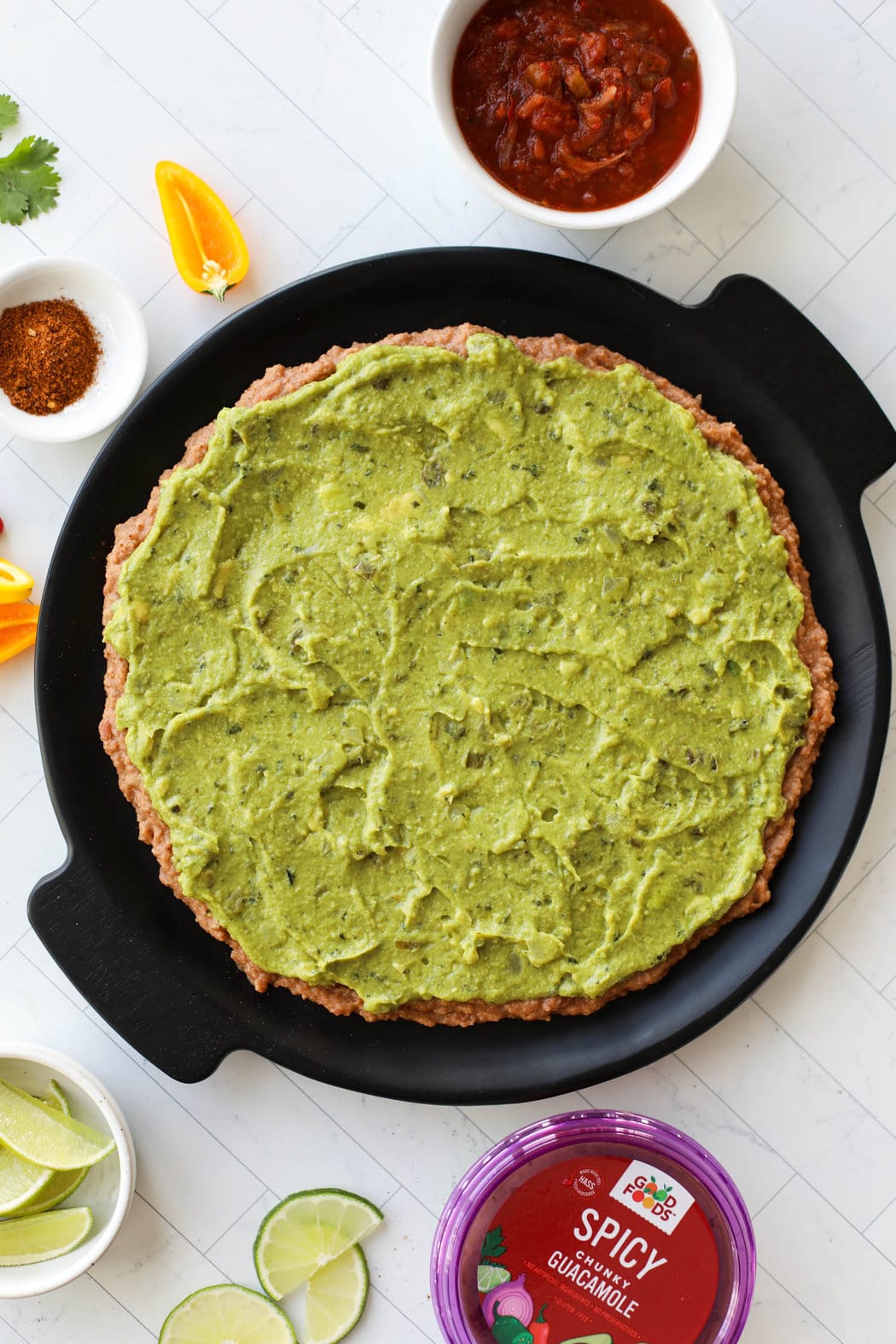 Black platter with layer of refried beans with guacamole spread in a circle.