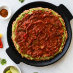Black round tray with layers of refried beans, guacamole, and salsa spread in a circle for 7 layer dip.