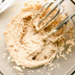 Peanut butter cream cheese whipped frosting in mixing bowl with hand mixer beaters.